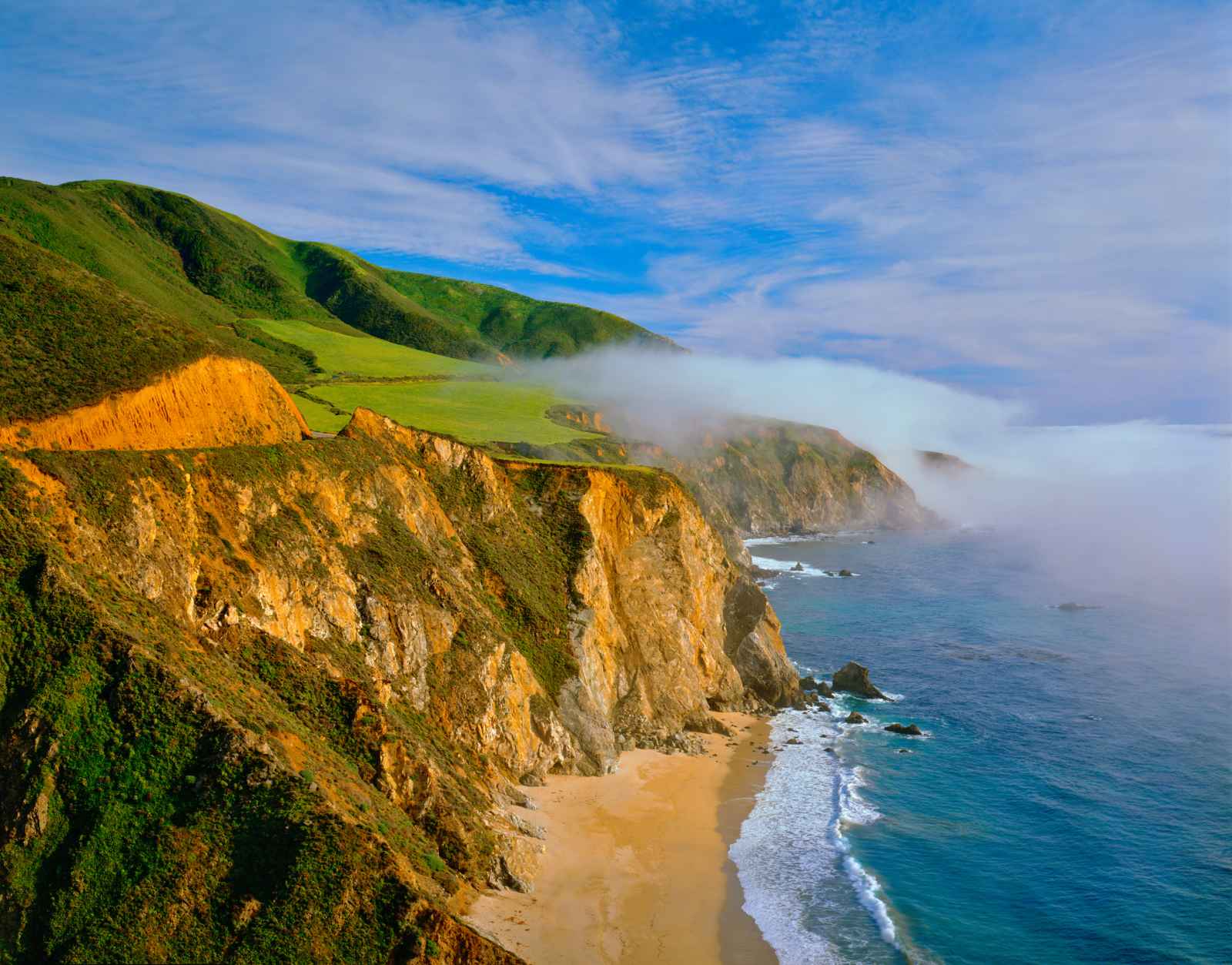 Big Sur coastal road with morning fog rolling over green hills
